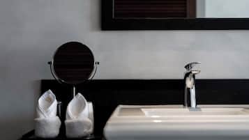 Un baño con un lavamanos blanco, un espejo redondo y dos toallas sobre una bandeja.
