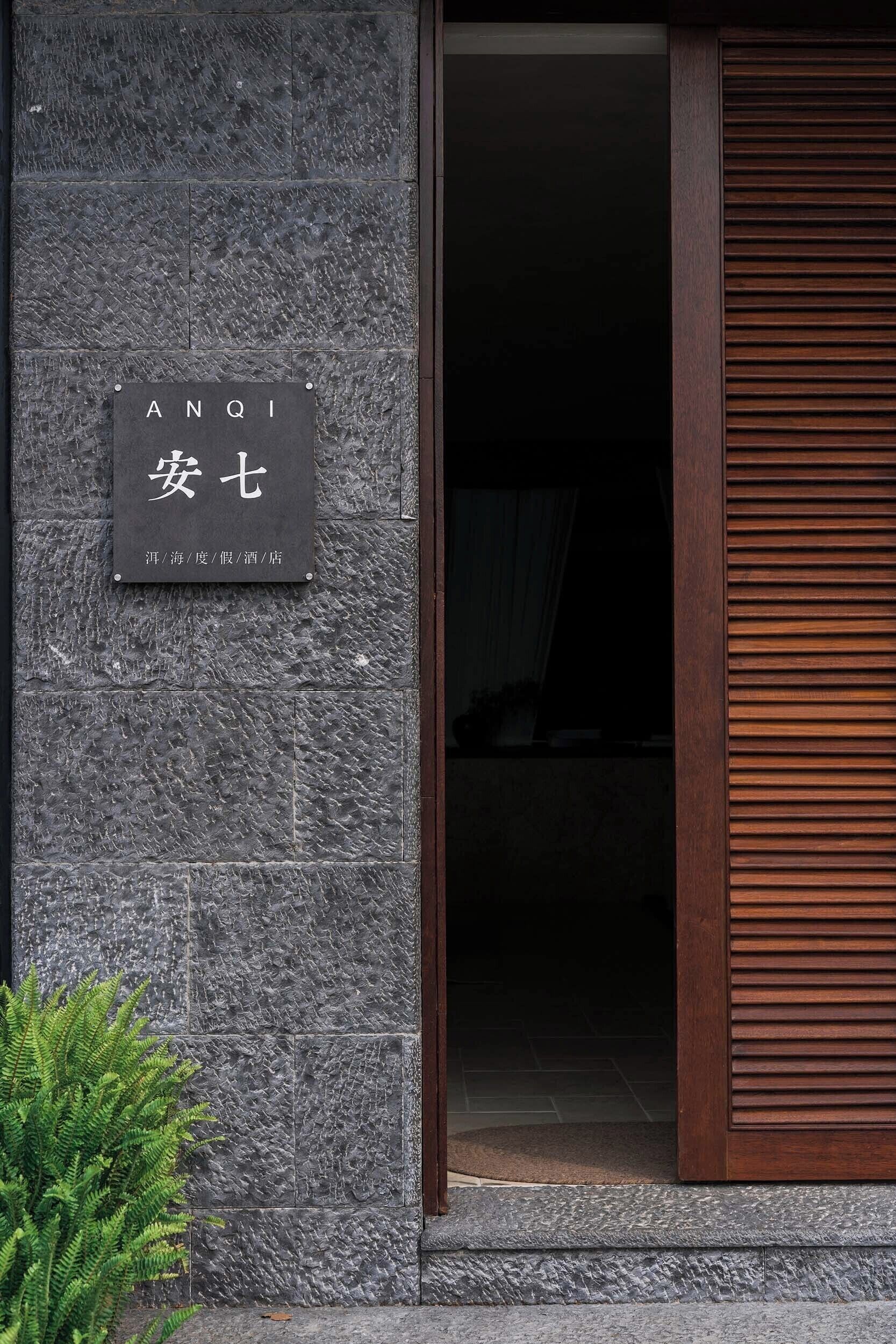 A stone wall with a sign reading "ANQI 安七" and a wooden door.