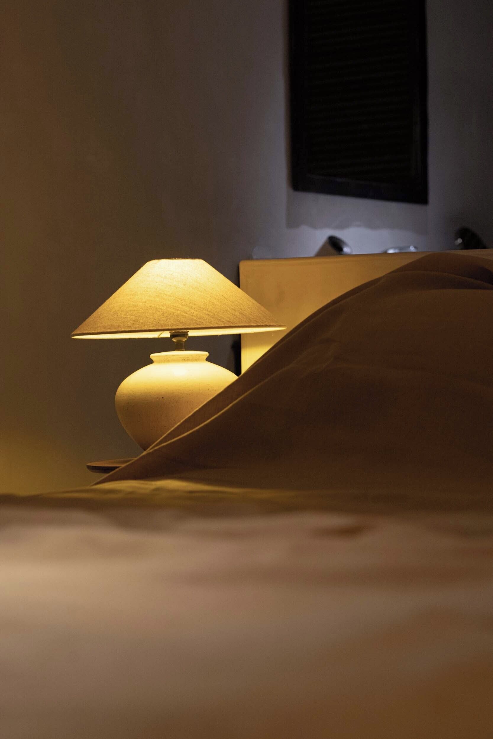 A bed with a lamp and a window with blinds.