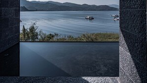 Un interior moderno con un amplio ventanal que da a una masa de agua tranquila y colinas lejanas.