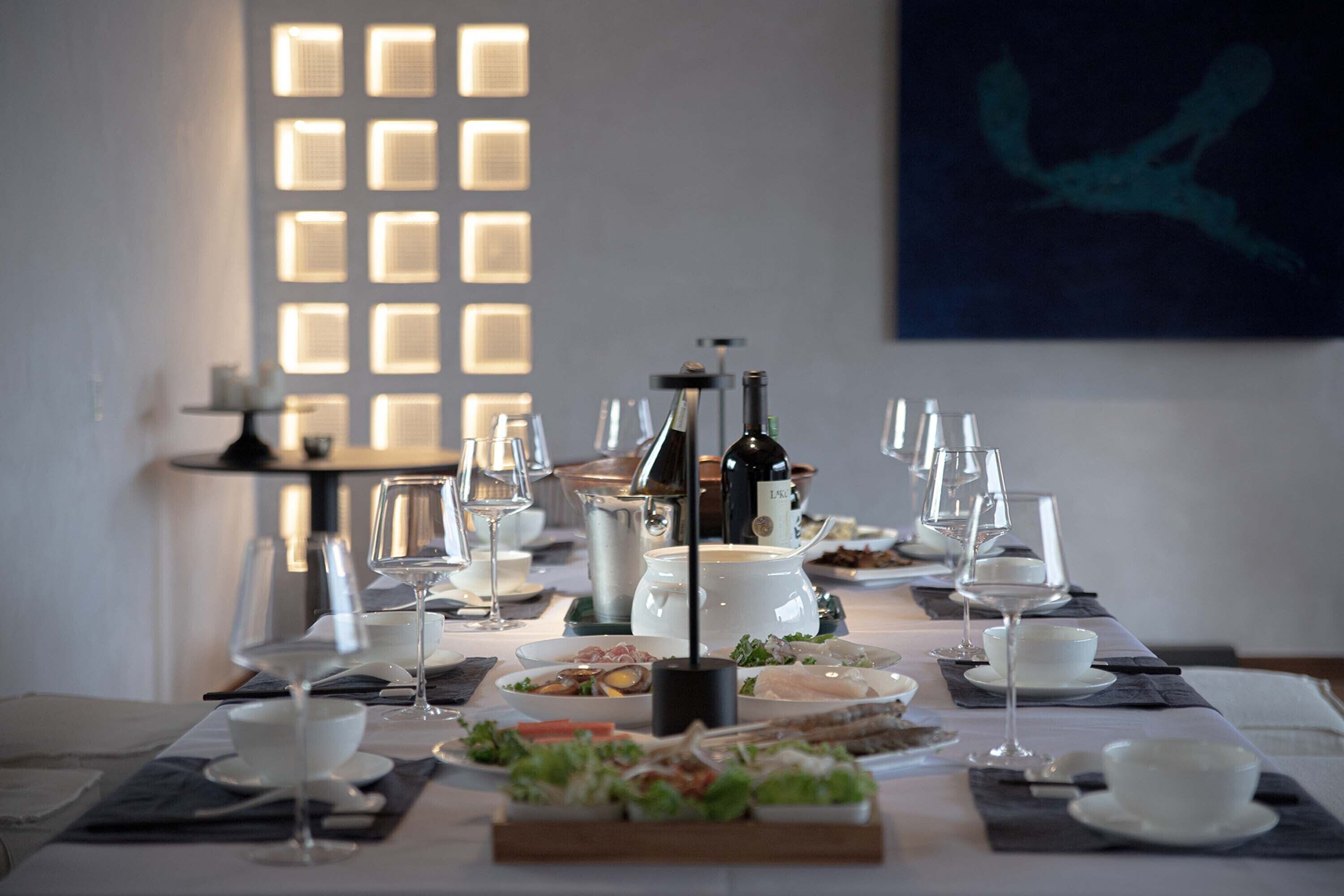 Une table à manger dressée pour un repas, avec des verres à vin, des assiettes et une bouteille de vin.