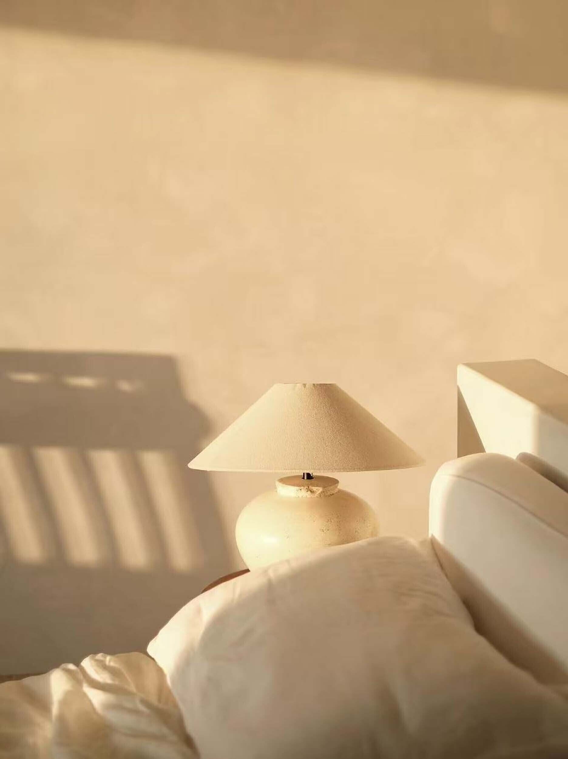 A bed with a white pillow and a white lamp with a beige shade.