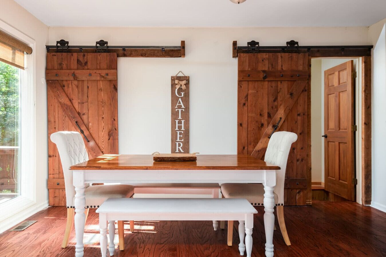 Un comedor con una mesa de madera, sillas blancas y un cartel con la palabra 'GATHER'.