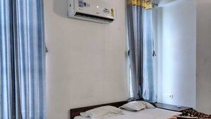 A bedroom with a bed, curtains, an air conditioning unit, and a ceiling fan. - Royal Galaxy Hotel (Shri Madhopur)