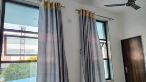 A room with two windows, each with grey curtains and a ceiling fan. - Royal Galaxy Hotel (Shri Madhopur)