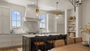 A modern kitchen with white cabinetry, a marble island, and pendant lighting. - Chateau Bleu: Desert Color Lagoon + Beaches (St. George)