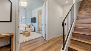 A modern interior with a wooden staircase, a living room with a sofa and TV, and a hallway leading to another room. - Chateau Bleu: Desert Color Lagoon + Beaches (St. George)