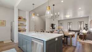 A modern kitchen with a central island, stainless steel appliances, and pendant lighting. - Chateau Bleu: Desert Color Lagoon + Beaches (St. George)