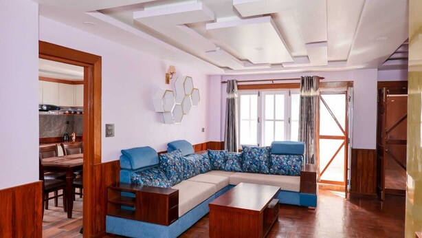 A modern living room with a sectional sofa, wooden flooring, and a dining area visible through an open door. - 3LDK, 2 private rooms, 1 shared room, spacious kitchen, meeting room, and parking space. (Nagarjun, Kathmandu, Bagmati)