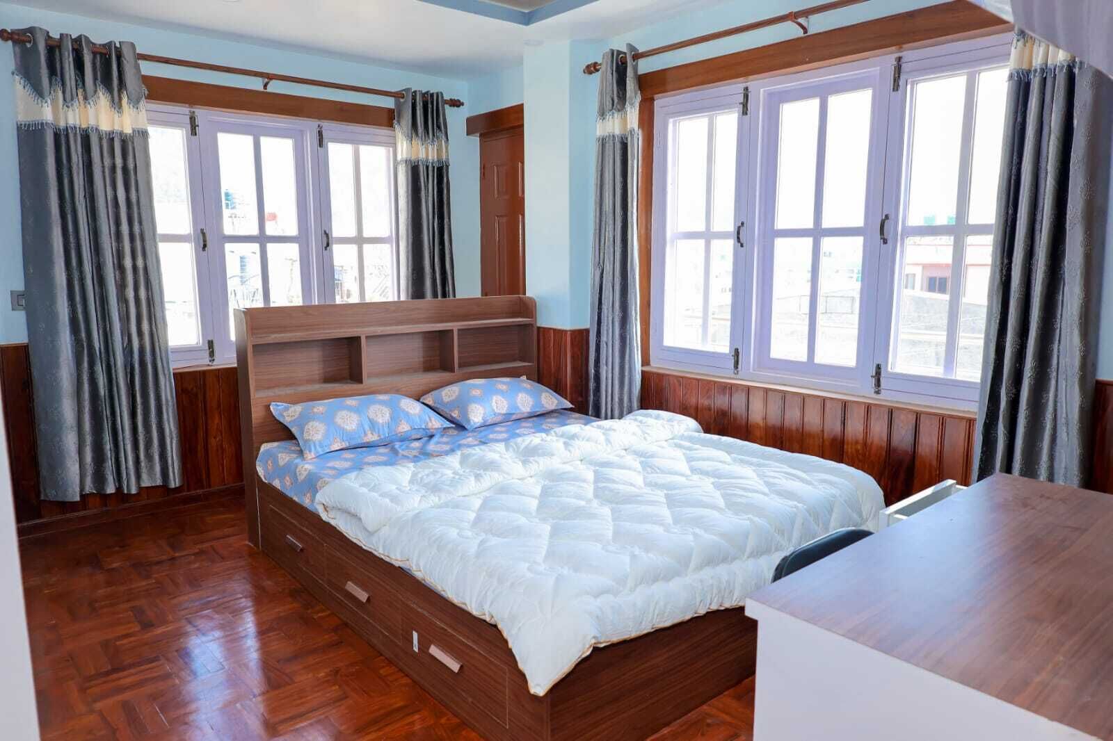 A bedroom with a wooden bed, two windows with curtains, and a wooden floor.
