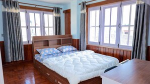 A bedroom with a wooden bed, two windows with curtains, and a wooden floor. - 3LDK, 2 private rooms, 1 shared room, spacious kitchen, meeting room, and parking space. (Nagarjun, Kathmandu, Bagmati)