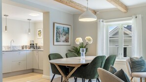 A modern kitchen with wooden beams, a dining area with green chairs, and a large window with curtains.