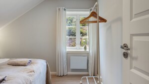 A bedroom with a bed, a window with curtains, a radiator, and a door.