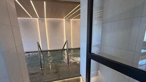 Un bagno moderno con vasca idromassaggio in vetro, pareti piastrellate e un design di soffitto elegante.