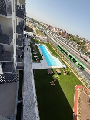 Hotel amb piscina, zona d'estar a l'exterior i vistes a un carrer animat amb un autobús verd.