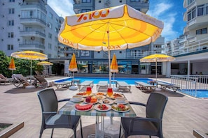 Un espace repas aménagé au bord de la piscine, avec des tables, des chaises et des parasols.