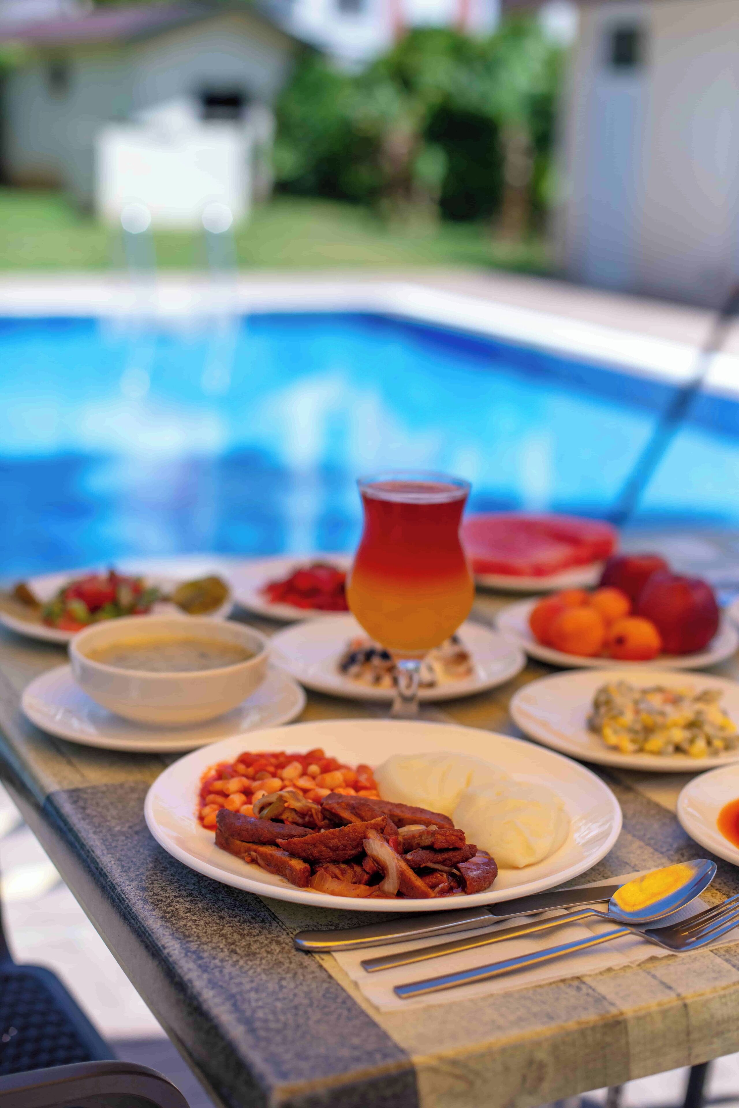 Mesa de comedor con varios platos y un vaso de bebida, con vista a una piscina.