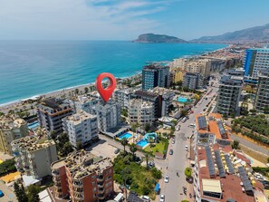 A coastal cityscape with high-rise buildings, a beach, and a red location marker. - BEST ALANYA OTEL (Alanya)