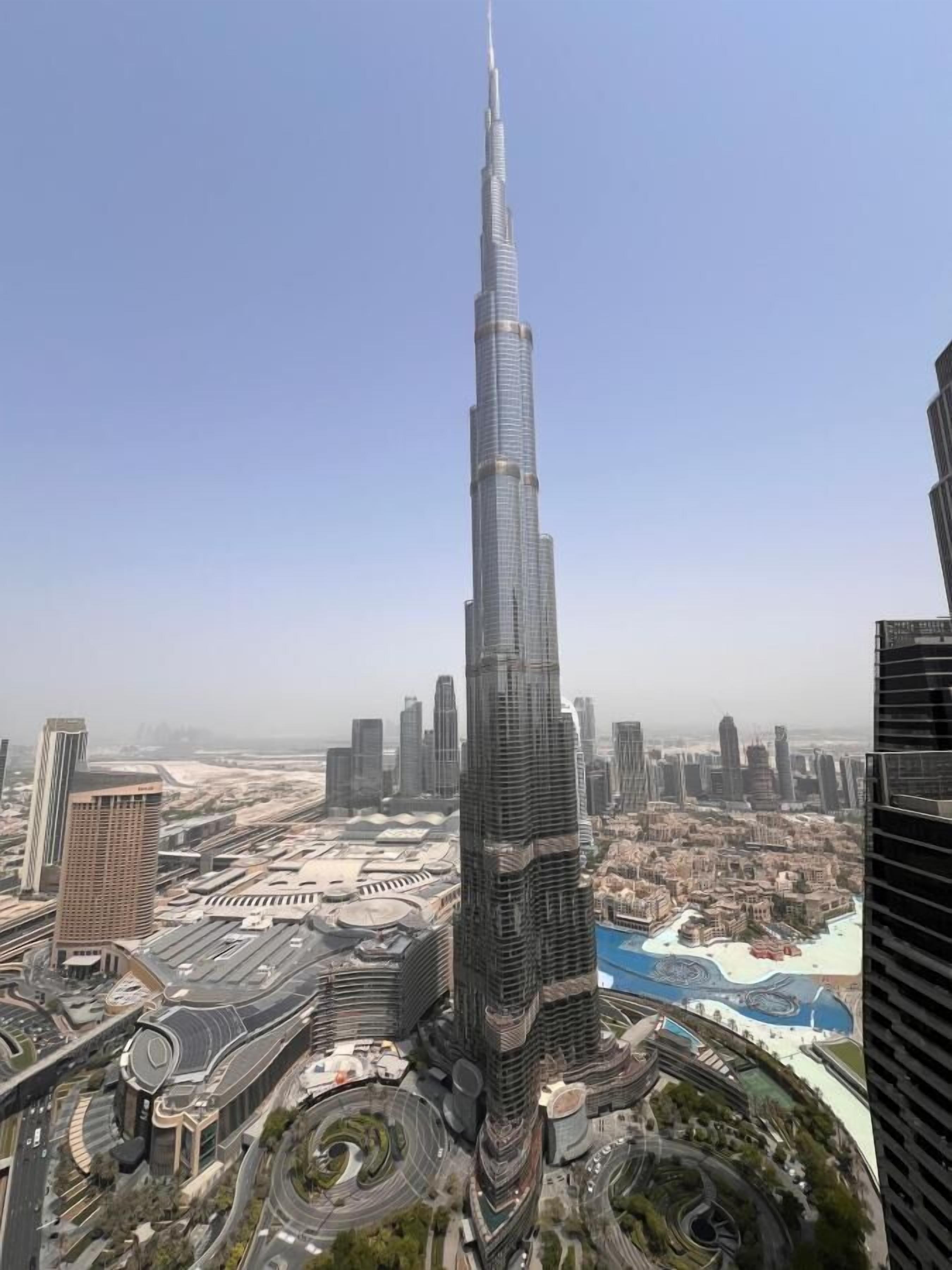 A high-rise building with a distinctive spire, surrounded by other modern skyscrapers and a complex urban layout.