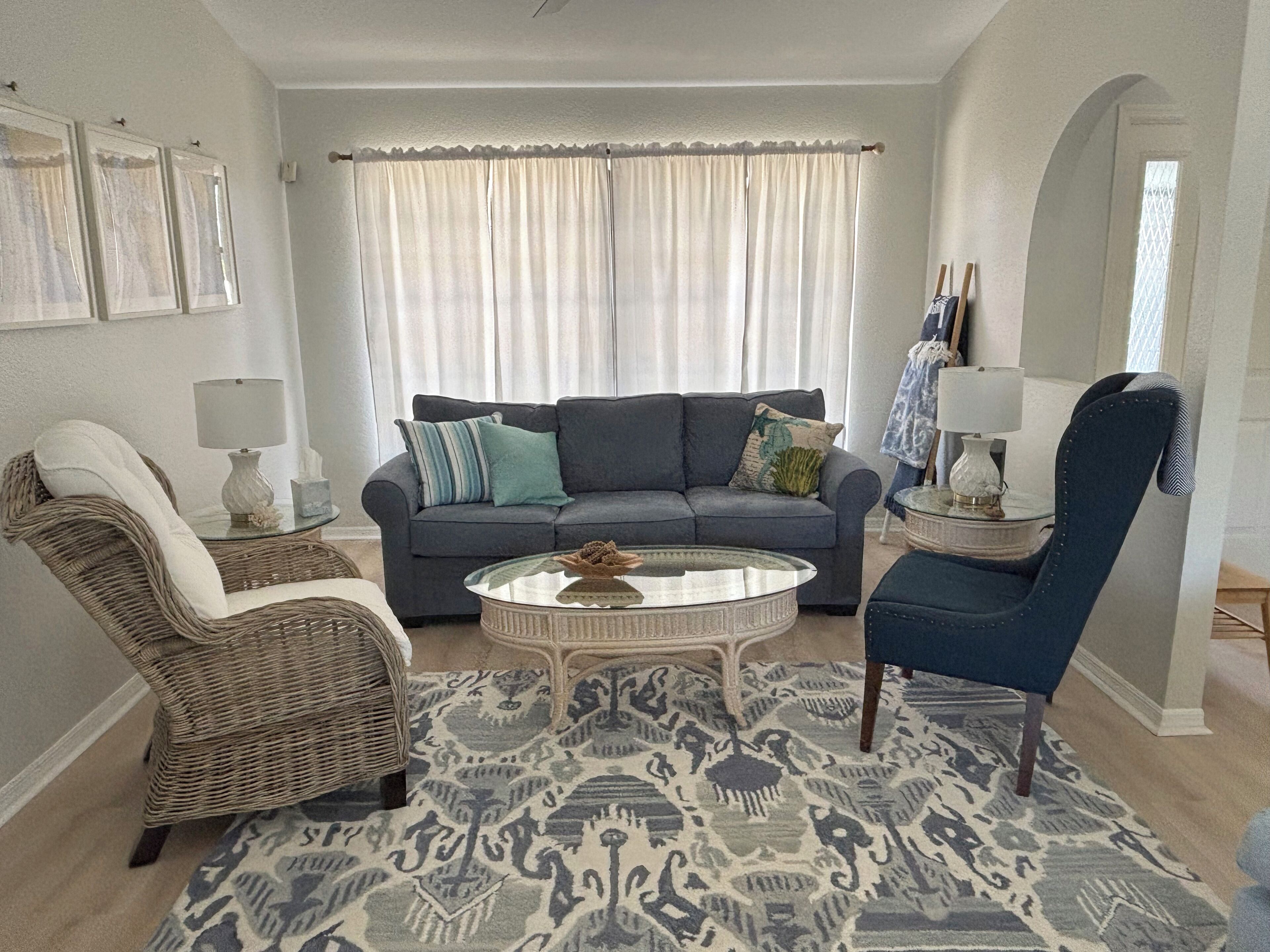 Ein Wohnzimmer mit grauem Sofa, zwei Sesseln, einem Couchtisch und einem gemusterten Teppich.