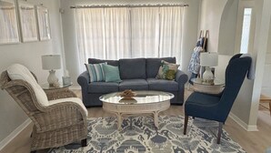 Un salon avec un canapé gris, deux fauteuils, une table basse et un tapis à motifs.
