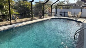 Une piscine aux eaux cristallines, entourée d’une paroi de verre, de plantes en pot et de mobilier d’extérieur.
