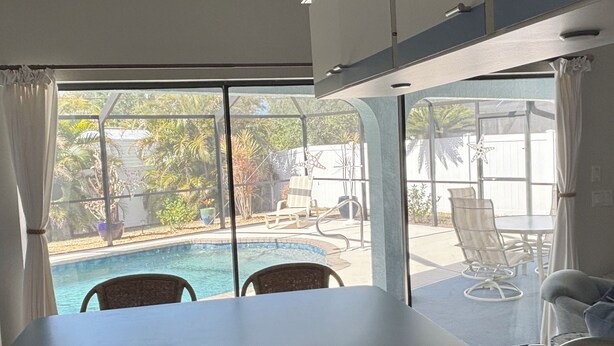 Une pièce dotée d’une grande fenêtre donnant sur une piscine, d’un coin repas avec une table et des chaises, et offrant une vue sur l’extérieur.