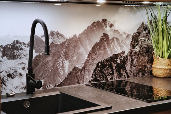 A kitchen with a modern faucet, a sink, and a decorative backsplash featuring a mountain landscape.