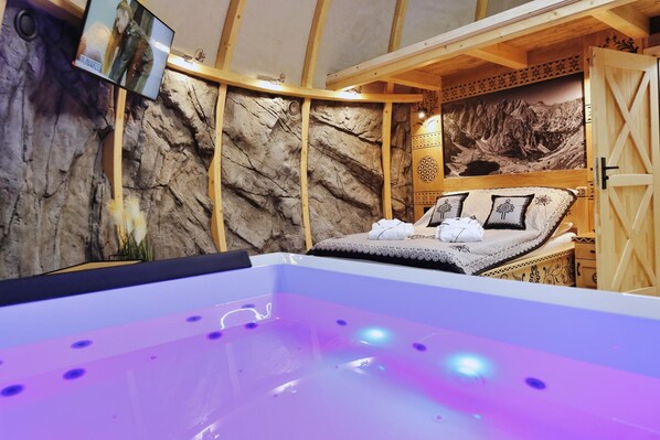 A spa room with a massage bed, a bathtub, and a wall with a rock-like texture. - Tatry Mountain Glamp z jacuzzi (Bukowina Tatrzanska)