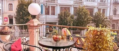Uma varanda com mesa e cadeiras, um abajur decorativo e vista para um edifício histórico.