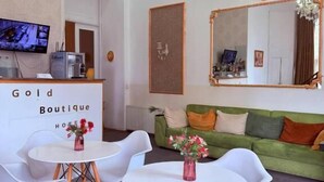 Una habitación de hotel moderna con una araña, un sofá verde, sillas blancas y una mesa con un florero.