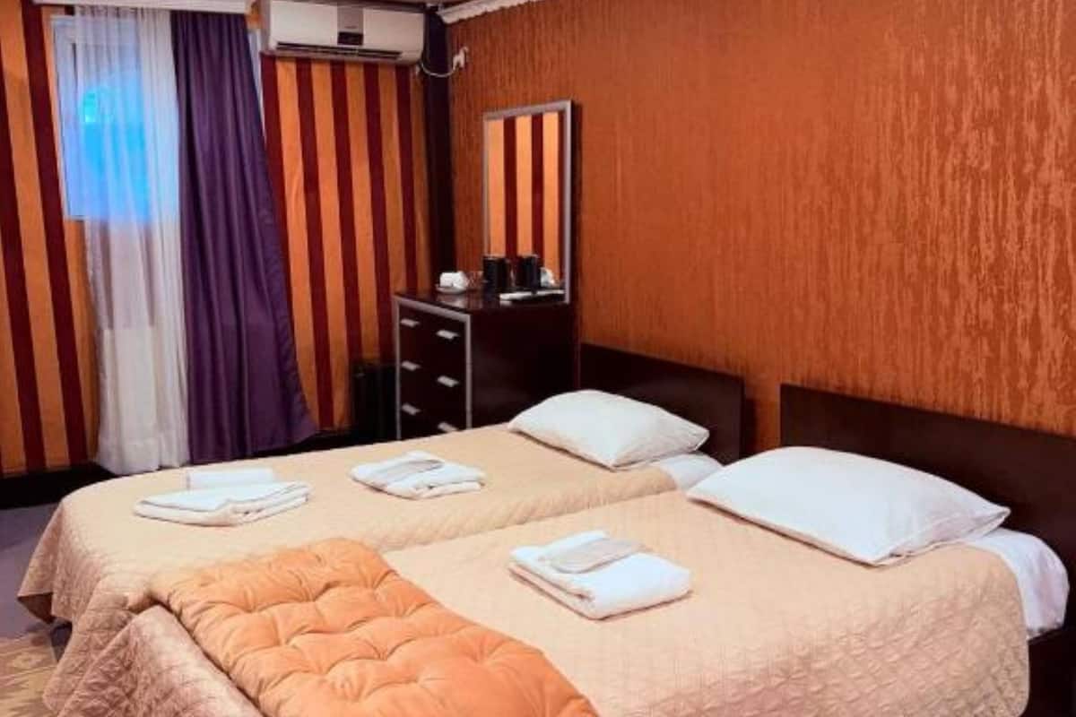 A hotel room with a large bed, a dresser, a mirror, and a window with curtains.