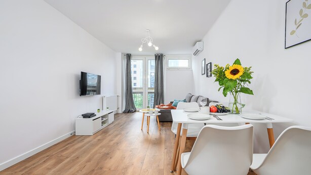 A modern living room with a flat-screen TV, a dining table with chairs, a sofa, and a large window with curtains. - ShortStayPoland Jana Pawla B90 (Warsaw)
