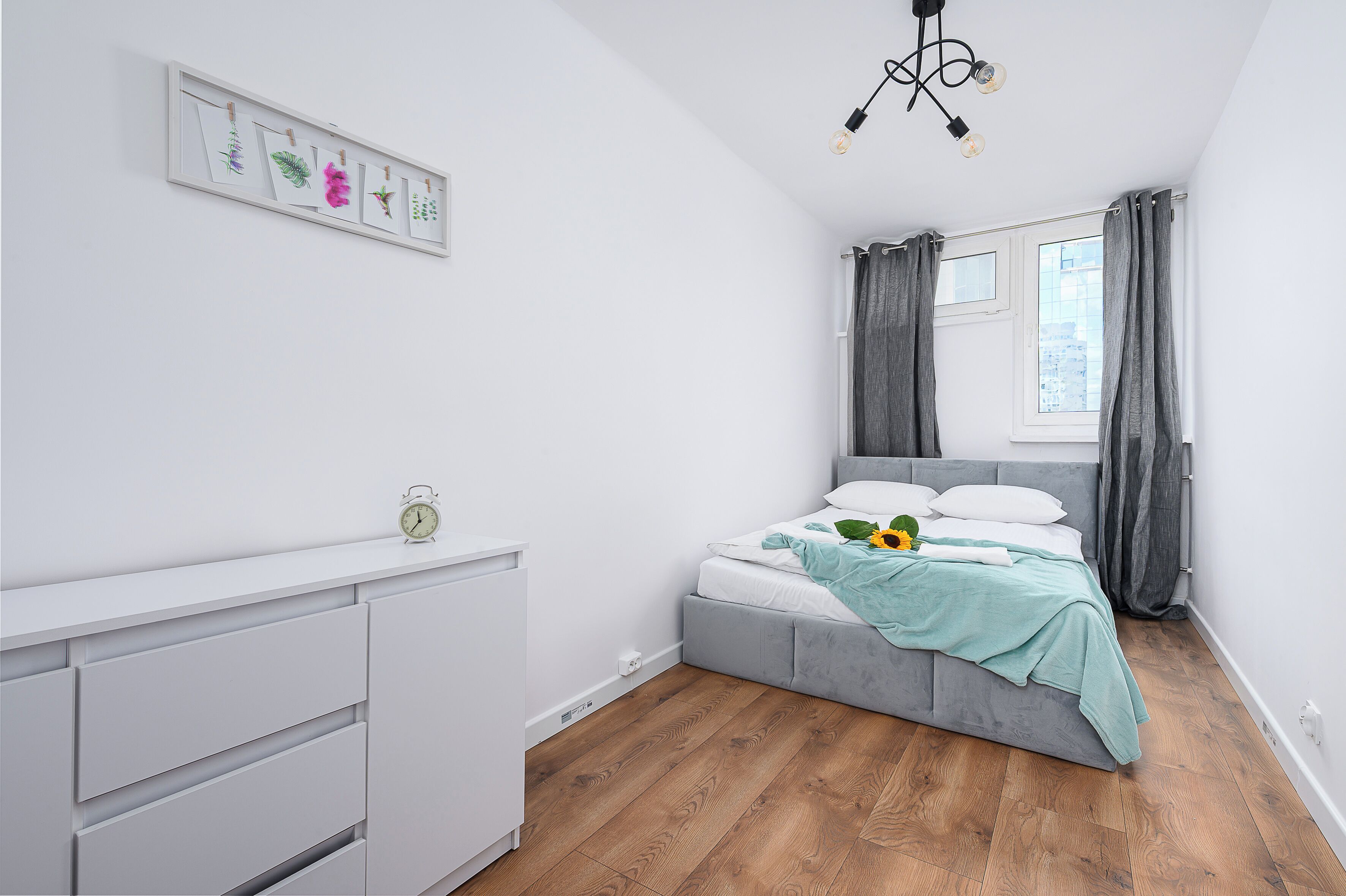 Een slaapkamer met een bed, een dressoir, een raam met gordijnen en een wandlamp.