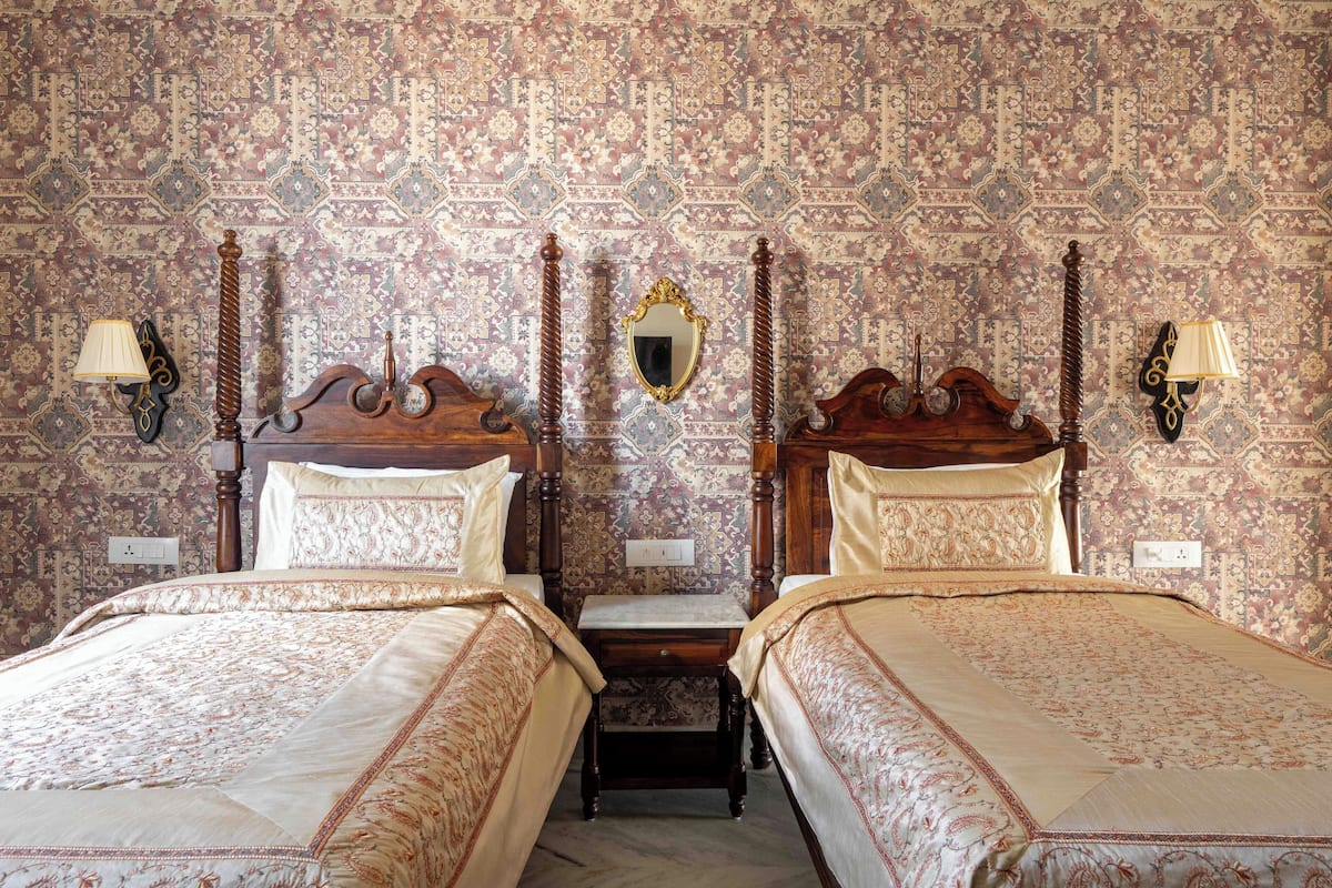 A room with two wooden beds, ornate headboards, a mirror, and patterned wallpaper.