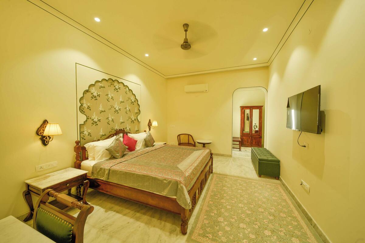 A bedroom with a bed, bedside table, lamp, chair, and a television.