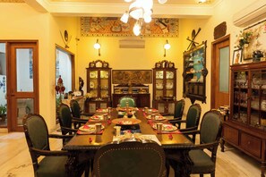 A dining room with a long table set for a meal, flanked by chairs, with traditional decor and a large painting on the wall.