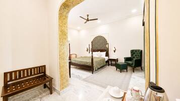 Un dormitorio con una cama con dosel, un sillón verde, un banco de madera y un espejo que refleja la habitación.