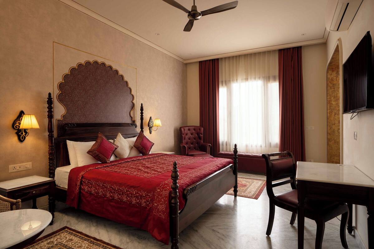 A hotel room with a large bed, a desk, a chair, a television, and a ceiling fan.