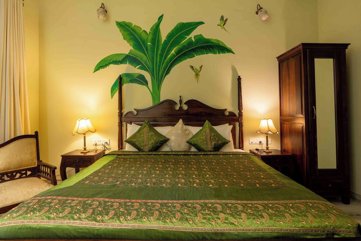 A neatly made bed with a green bedspread, two bedside lamps, a wooden nightstand, a chair, and a large mirror on the wall.