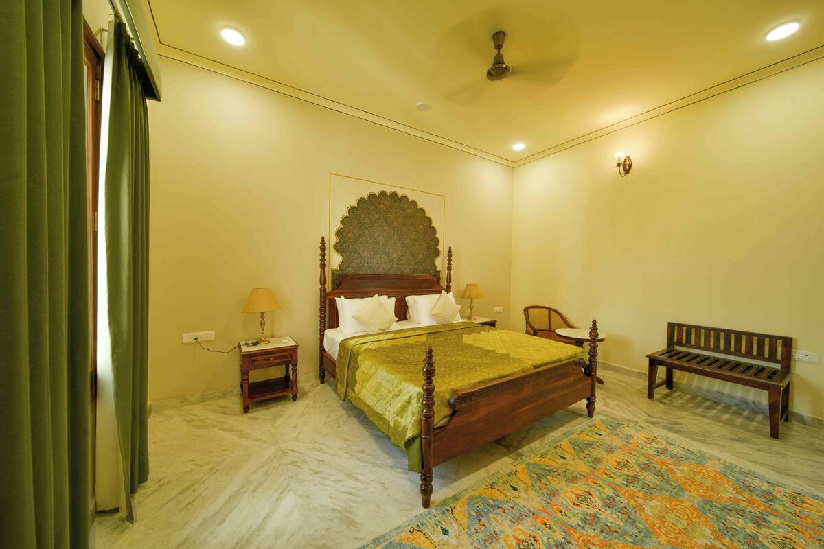 A bedroom with a four-poster bed, a bench, a nightstand, and a wall-mounted lamp.