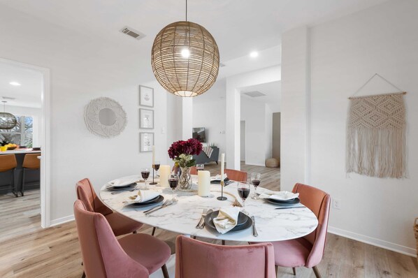 A dining area with a round table, pink chairs, a woven pendant light, and a macrame wall hanging. - Long-Term Stays Only | 29 Night Mins | Walk to MF (Marble Falls)