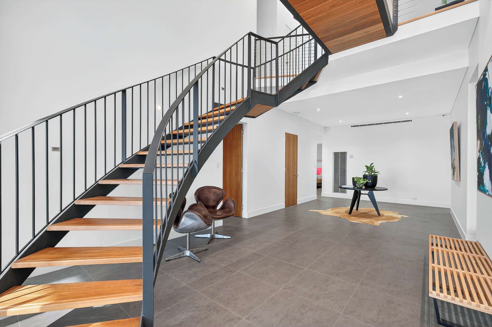 Un interior moderno con una escalera espiral, un sillón de cuero, una mesa redonda con una planta y un banco de madera.