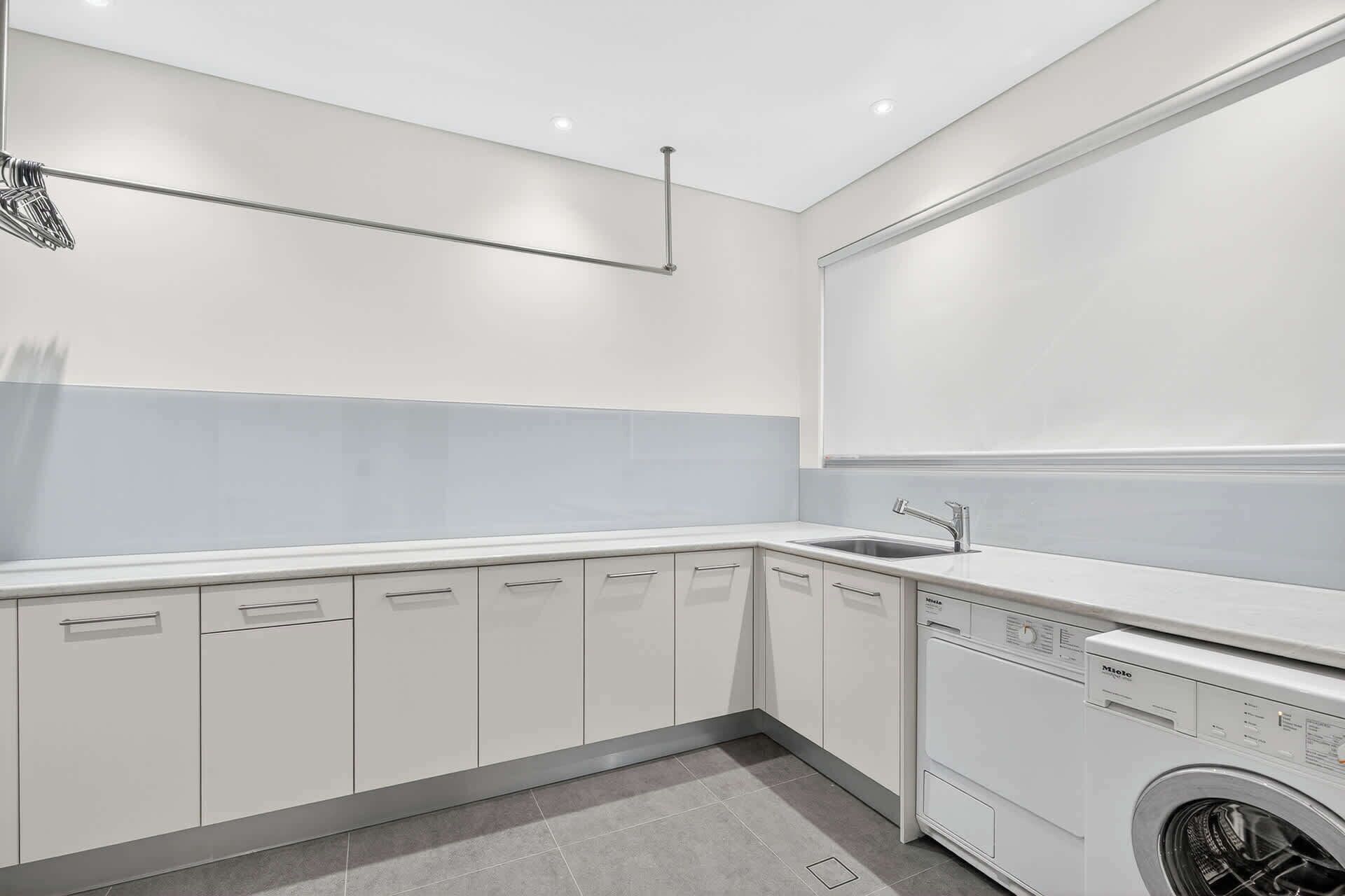 A modern kitchen with white cabinets, a built-in washing machine, and a large window.