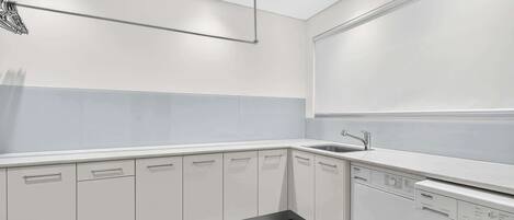 A modern kitchen with white cabinets, a built-in washing machine, and a large window.