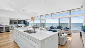 A modern kitchen with a large island, dining area with chairs, and a sofa with a view of the sea. - 7 Boomer Drive, Port Elliot (Port Elliot)