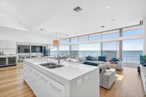 A modern kitchen with a large island, dining area with chairs, and a sofa with a view of the sea. - 7 Boomer Drive, Port Elliot (Port Elliot)