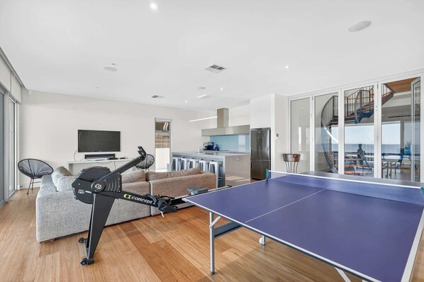 A modern living room with a ping pong table, exercise equipment, a sofa, and a kitchen area. - 7 Boomer Drive, Port Elliot (Port Elliot)