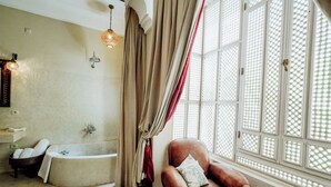 Une pièce avec une baignoire, un fauteuil en cuir et une fenêtre ornée d’un motif en croisillons.