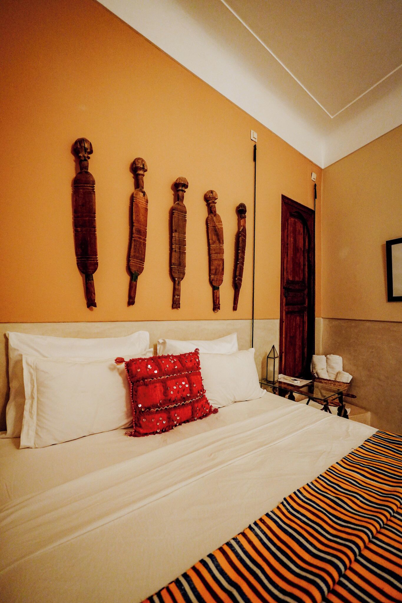 Una cama con almohadas blancas y rojas, una colcha a rayas y adornos de madera en la pared.